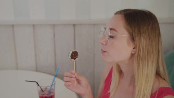 Mooi jong meisje zit aan een tafel in een café en eet zoete verse desserts van een bord. — Stockvideo