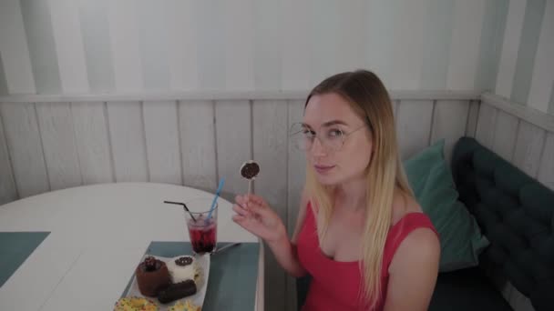 La bella ragazza si siede a un tavolo in un caffè e mangia dolci dessert freschi da un piatto . — Video Stock