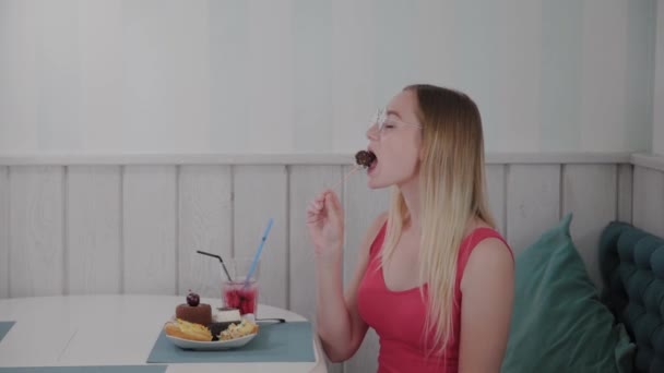 Mooi jong meisje zit aan een tafel in een café en eet zoete verse desserts van een bord. — Stockvideo