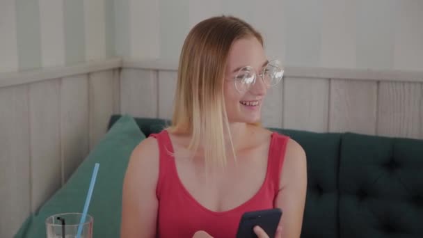 Una joven hermosa utiliza un teléfono móvil en un restaurante en una mesa, a su alrededor es un plato con postres . — Vídeo de stock