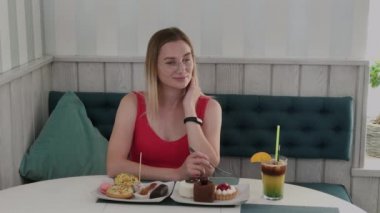 Güzel genç kız bir kafede bir masada oturur ve bir tabak tatlı taze tatlılar yiyor.