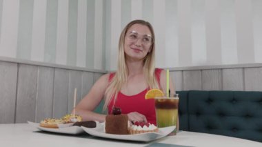 Güzel genç kız tatlılar bir tabak ile bir kafede bir masada oturan.