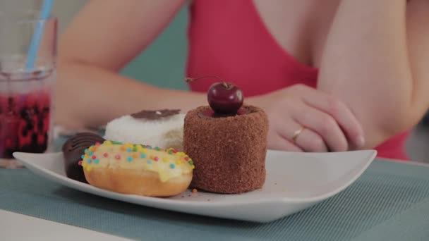 Piękna młoda dziewczyna siedzi przy stole w kawiarni i zjada słodkie świeże desery z talerza. — Wideo stockowe