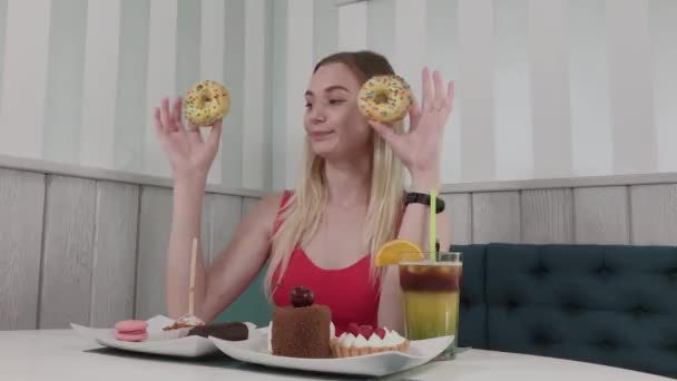Όμορφο κορίτσι που ποζάρει με ντόνατς στα χέρια σε ένα τραπέζι σε ένα καφέ. — Αρχείο Βίντεο