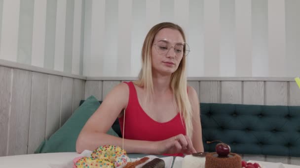 Hermosa joven se sienta en una mesa en un café y come dulces postres frescos de un plato . — Vídeos de Stock