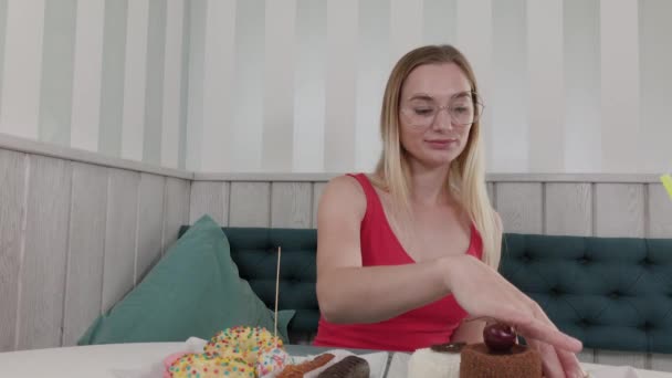 Belle jeune fille assise à une table dans un café et mange des desserts frais sucrés d'une assiette . — Video