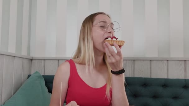 Hermosa joven se sienta en una mesa en un café y come dulces postres frescos de un plato . — Vídeos de Stock