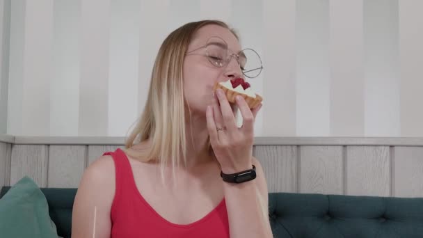 Hermosa joven se sienta en una mesa en un café y come dulces postres frescos de un plato . — Vídeos de Stock