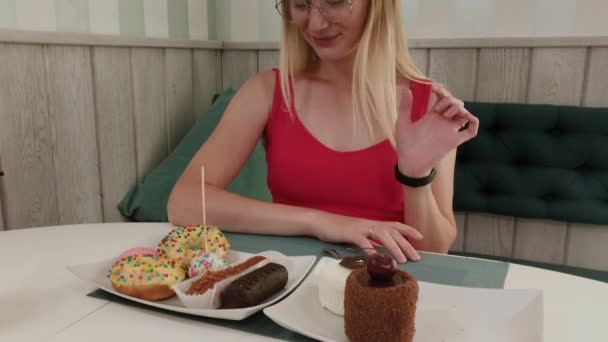 Belle jeune fille assise à une table dans un café et mange des desserts frais sucrés d'une assiette . — Video