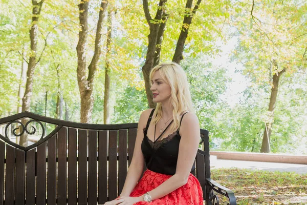 Mooie vrouw zit op een bankje in een park. — Stockfoto