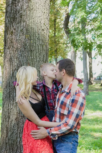 Belos abraços familiares jovens felizes por uma árvore no parque . — Fotografia de Stock
