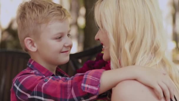 Schöner kleiner Junge schenkt seiner geliebten Mutter im Park auf einer Bank einen Blumenstrauß. — Stockvideo