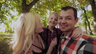 Mutlu neşeli aile sarılma ve parkta ağaç tarafından gülümseyen.