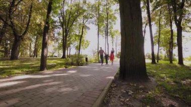 Mutlu genç aile sokak boyunca parkta yürüyor.