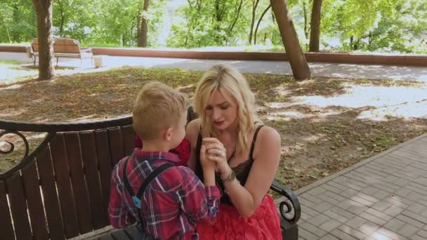 Mooie kleine jongen geeft een boeket bloemen aan zijn geliefde moeder in het Park op een bankje. — Stockvideo