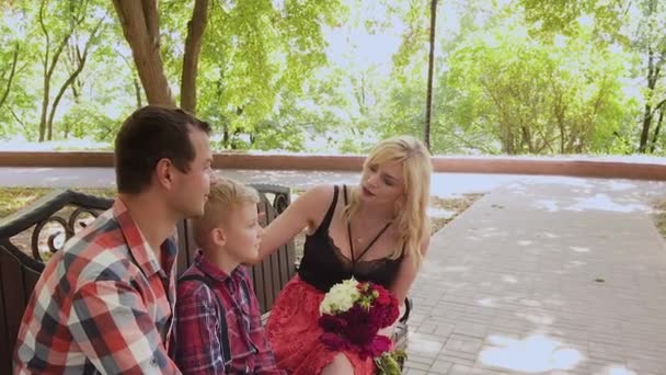 Hermosa familia sentada en un banco en el parque y hablando . — Vídeos de Stock