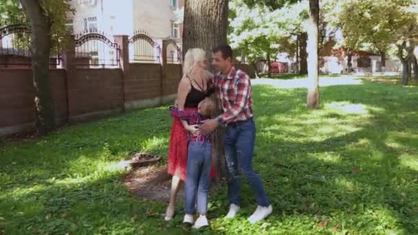 Fröhliche fröhliche Familie, die sich am Baum im Park umarmt und lächelt. — Stockvideo
