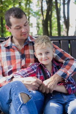 Yakışıklı baba ve oğlu parkta bir bankta oturuyorlar..