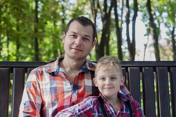 Schöner Vater und Sohn sitzen auf einer Bank im Park. — Stockfoto