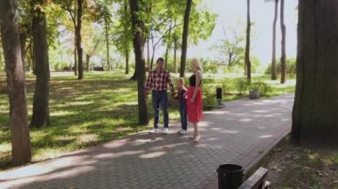 Mutlu genç aile sokak boyunca parkta yürüyor.