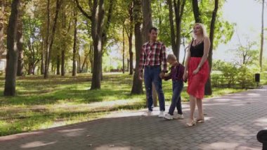 Mutlu genç aile sokak boyunca parkta yürüyor.