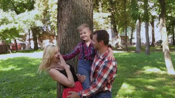 Feliz familia alegre abrazando y sonriendo por el árbol en el parque . — Vídeo de stock