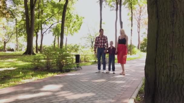 Happy young family walks in the park along the alley. — Stock Video