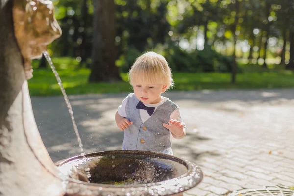 Beautiful little boy plays with a stream of water in the park. — Stock Photo, Image