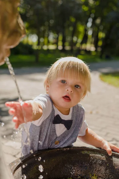 Beautiful little boy plays with a stream of water in the park. — Stock Photo, Image