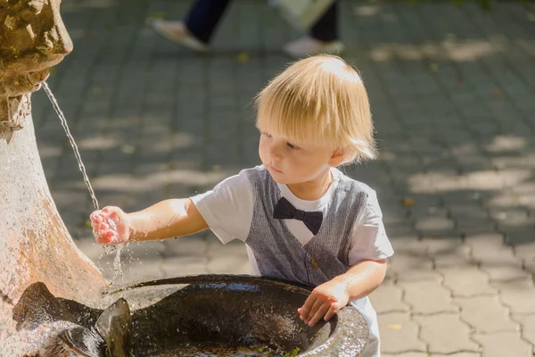 Beautiful little boy plays with a stream of water in the park. — Stock Photo, Image