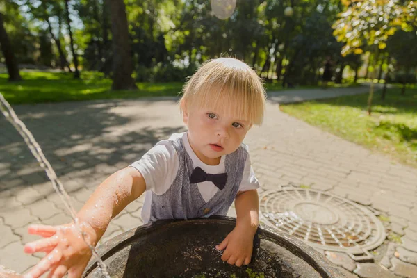 Beautiful little boy plays with a stream of water in the park. — Stock Photo, Image