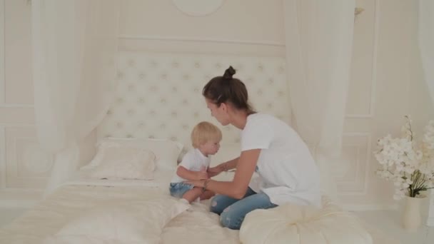 Schöne glückliche Mutter und Sohn spielen auf dem weißen Bett. — Stockvideo
