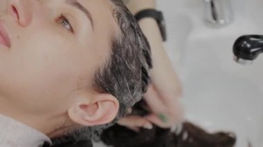 Kız kuaför müşterinin kafasına şampuan koyar..