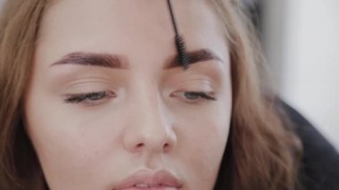 Profesyonel makyaj sanatçısı güzel bir kız özel bir kaş fırçası ile kaştarama. Güzellik salonunda kaş makyajı yapan kadın müşteri.