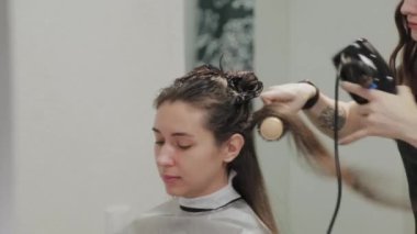 Kız kuaför kuaförde saç kurutma makinesiyle müşteriye saç kurutur..