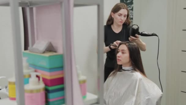 Peluquería chica seca el cabello al cliente con secador de pelo en la peluquería . — Vídeos de Stock