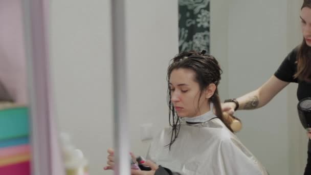 女の子の美容師は、美容師でヘアドライヤーでクライアントに髪を乾かします. — ストック動画