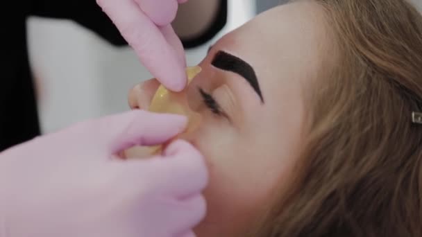 Makeup καλλιτέχνης βάζει μια χρυσή μάσκα κάτω από τα μάτια του πελάτη. — Αρχείο Βίντεο