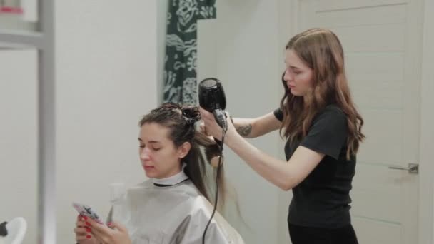 Peluquería chica seca el cabello al cliente con secador de pelo en la peluquería . — Vídeos de Stock