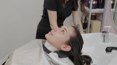 Kuaför salonu. Bir kuaför, müşterilerinin saçlarını yıkadıktan sonra havluyla lavaboya siliyor..