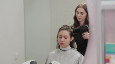 Kız kuaför kuaförde saç kurutma makinesiyle müşteriye saç kurutur..