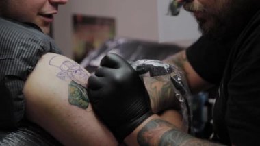 Profesyonel dövme sanatçısı bir adamın kolunda dövme yapar..