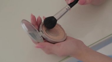 Kadın elleri makyaj fırçasını barutla yakın plan bir kapta tutuyor..