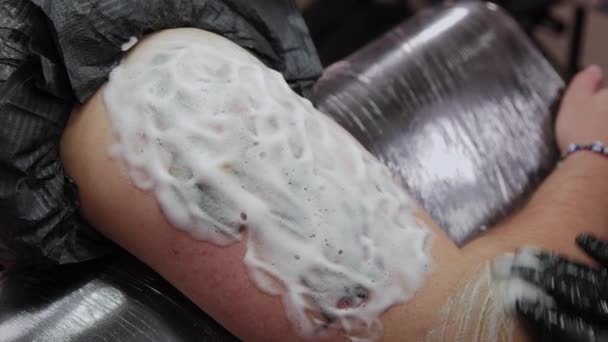 Un homme est assis dans un salon de tatouage avec de la mousse sur un tatouage . — Video