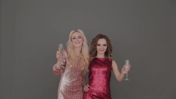Två unga och vackra flickor på en grå bakgrund med glas champagne i händerna. — Stockvideo