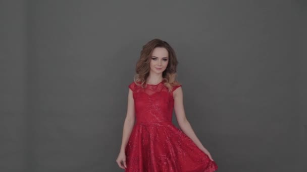 Beautiful young girl in a red dress posing on a gray background.