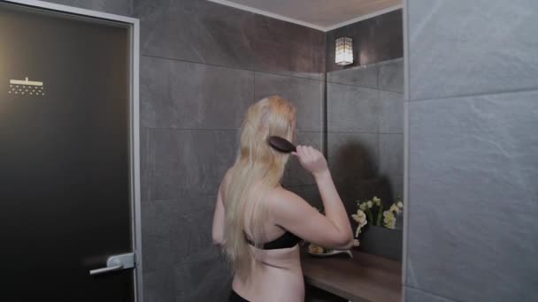 Menina bonita em um maiô penteando seu cabelo pelo espelho . — Vídeo de Stock