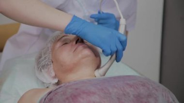 Profesyonel kozmetoloji ofisinde mikroakımlı yaşlı bir kadın için işlem yapar.