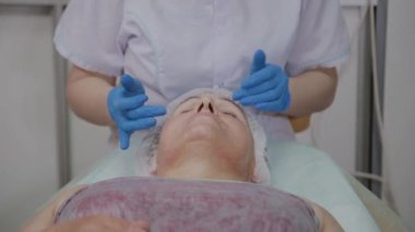 Profesyonel kozmetolojist güzellik salonunda yaşlı kadın için koruyucu krem uygular.