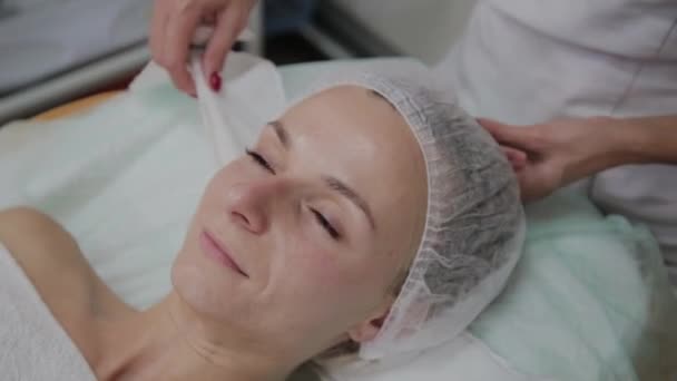 Professionele schoonheidsspecialiste past de beschermende hoofddeksels van de patiënt aan. — Stockvideo